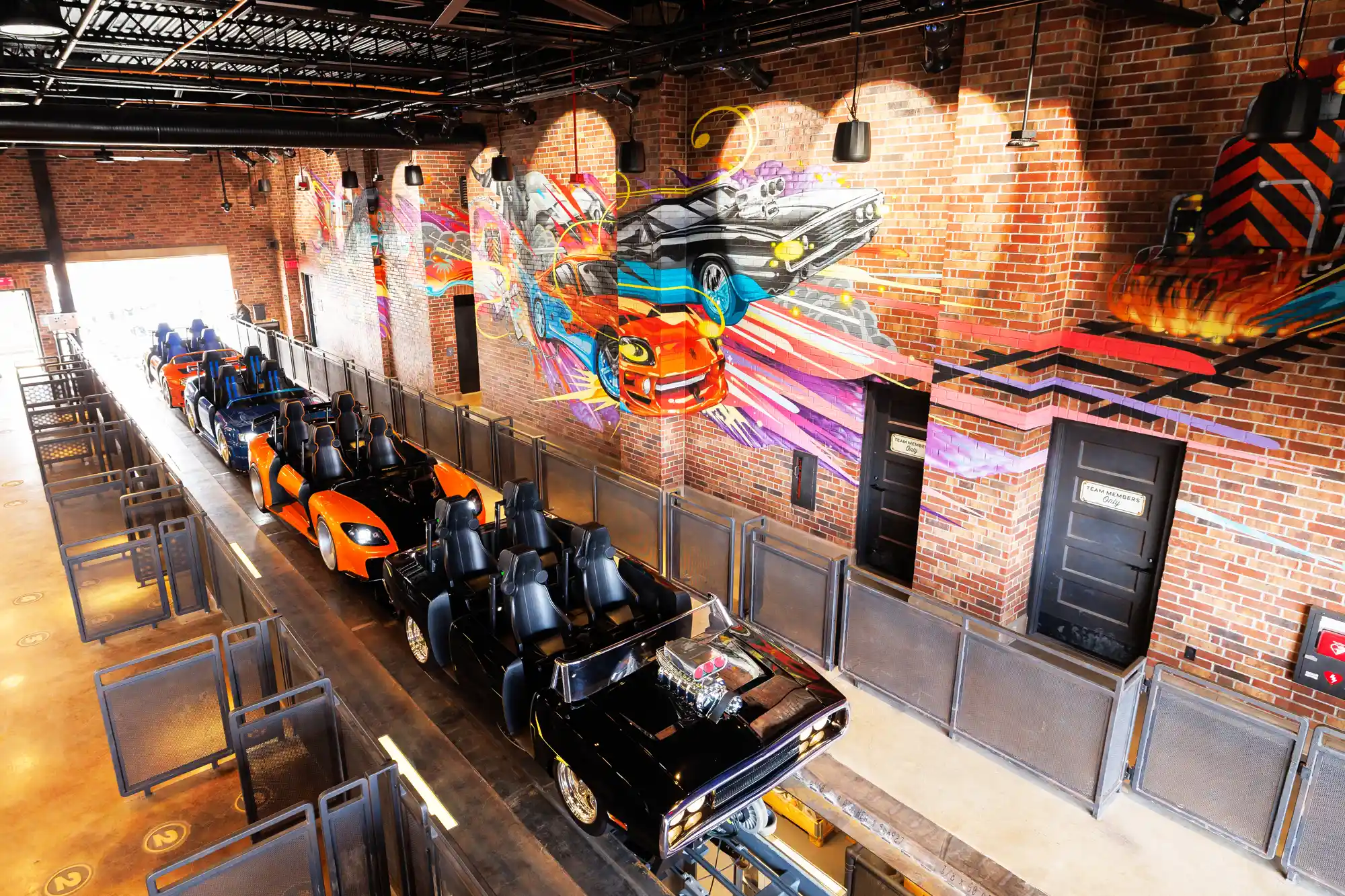 Vibrant mural of race cars on brick wall above empty ride vehicles in the load station at a theme park attraction. This new ride will be at both Universal Parks in the USA.