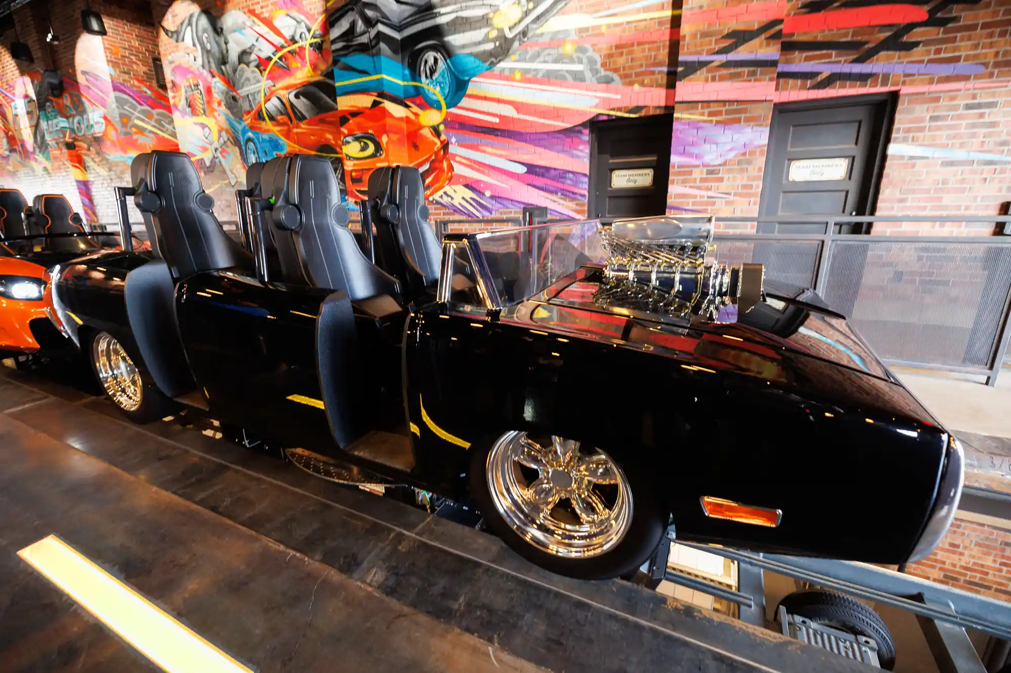 Themed muscle car ride vehicle with four seats inside a vibrant, mural-filled show building at an immersive attraction.