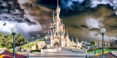 An enchanting castle towers at the center of the park, framed by stormy skies and lightning for a thrilling fairytale adventure. Disney Parks weather disruption.