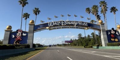 Iconic Walt Disney World entrance arch featuring Minnie and Mickey Mouse, framed by palm trees under a bright blue sky.