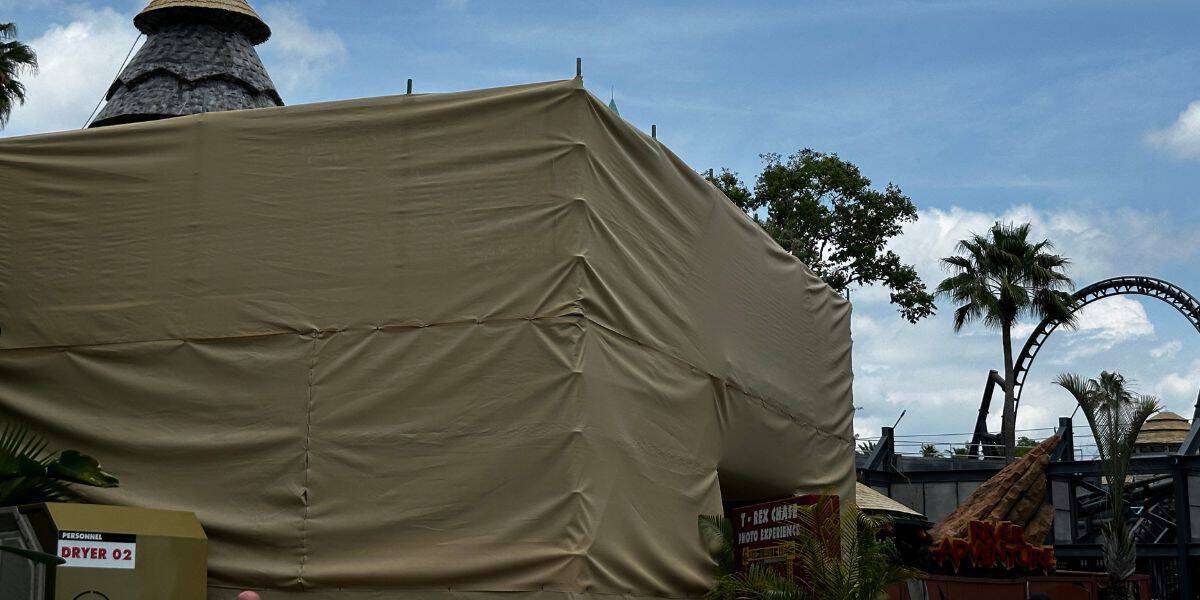 A tan construction tarp covers part of Universal Studios, with palm trees and Velocicoaster in the background.