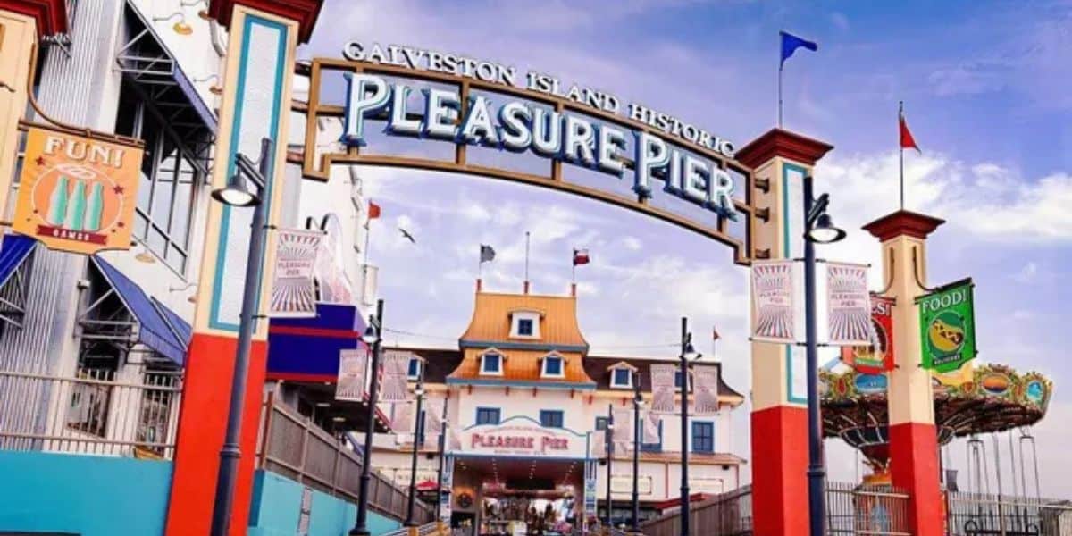 Galveston Island Historic Pleasure Pier entrance with vibrant signage, roller coaster, and exciting rides beckoning thrill-seekers.