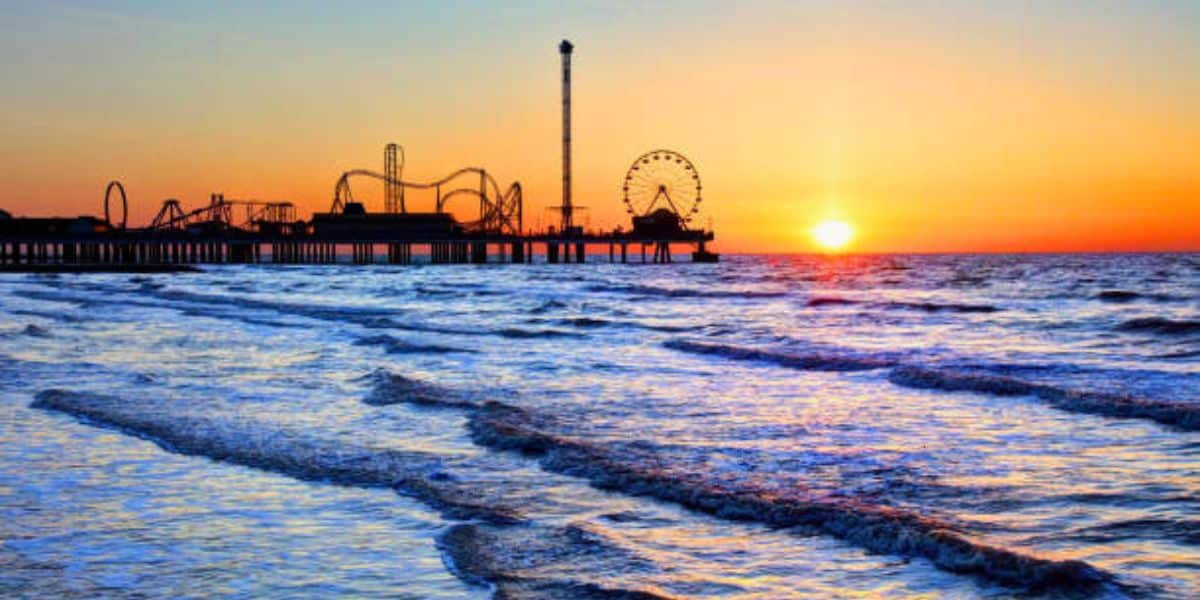 Santa Monica Pier at sunset, showcasing the Pacific Park roller coaster and Ferris wheel silhouetted against a glowing sky.