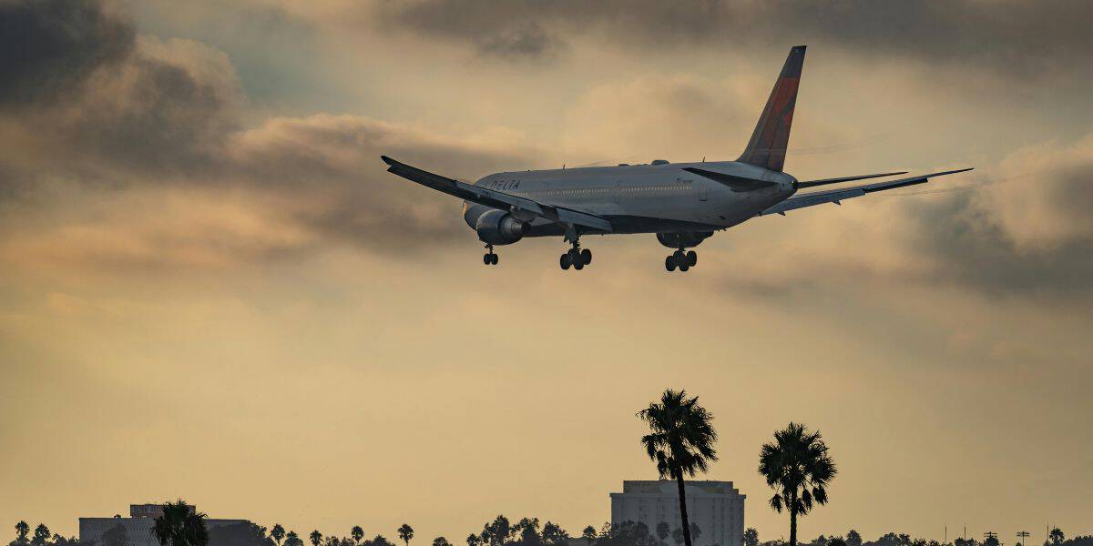 A plane descends at sunset over palm trees and resort hotels, evoking the excitement of arriving for a theme park adventure.