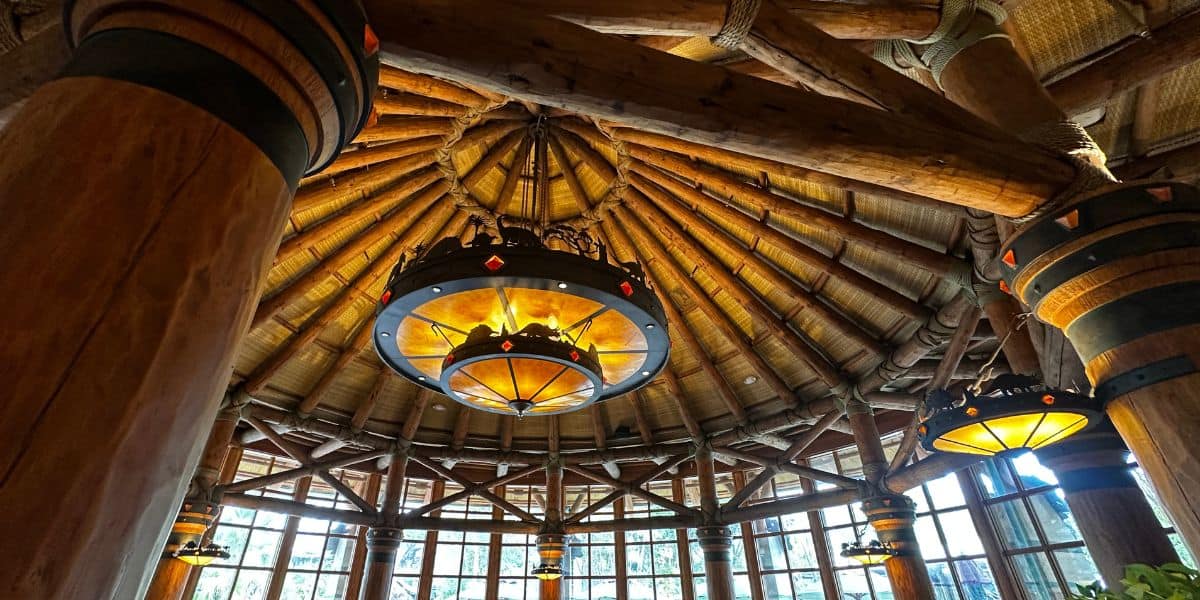 Rustic lodge ceiling at a theme park resort, with grand circular chandeliers and sunlight pouring through towering windowsRustic lodge ceiling at a theme park resort, with grand circular chandeliers and sunlight pouring through towering windows.
