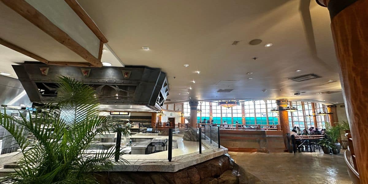Lively dining hall with themed buffet station, whimsical decor, and guests enjoying views of parade floats through grand windows. at Thunder Falls Terrance inside Jurassic Park at Islands of Adventure at Universal Orlando. 