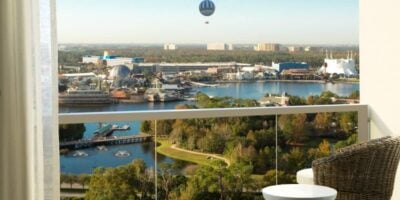 Balcony view of a lake, lush trees, and Disney World with a hot air balloon—ideal for theme park fans visiting Orlando. Disney Springs prices.