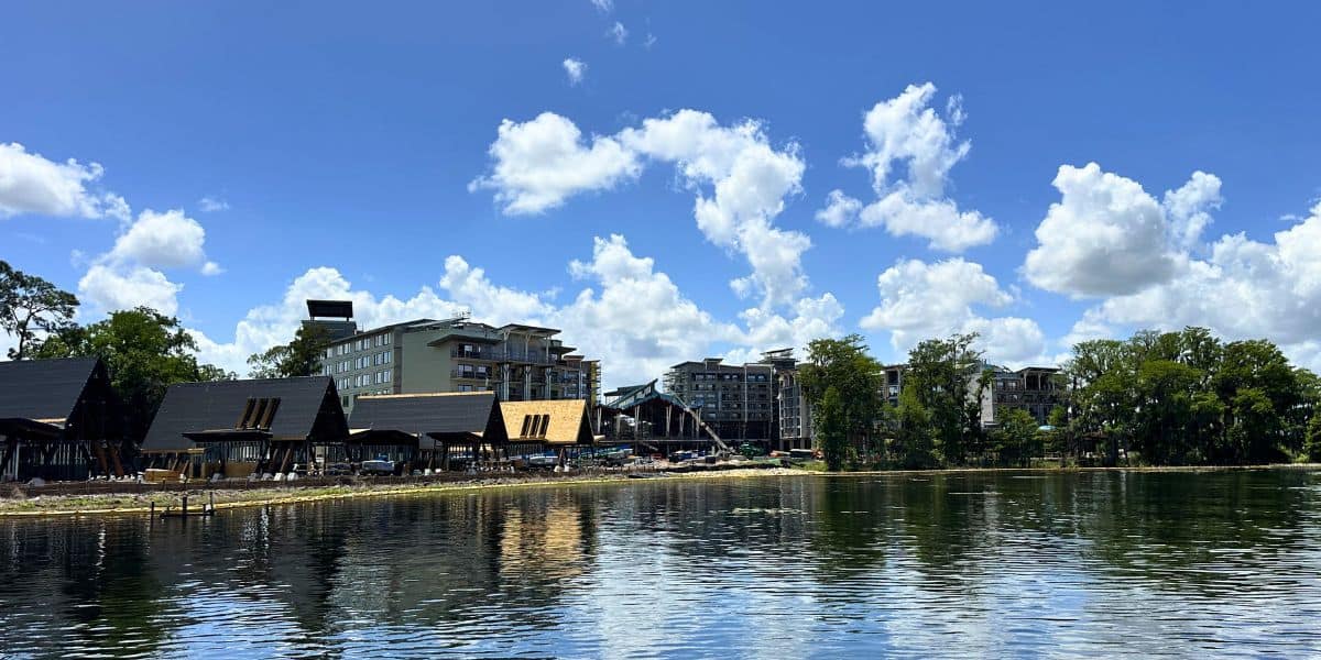 A serene lake mirrors lush trees and resort buildings under a sunny sky at Disney Orlando’s latest guest-exclusive retreat.
