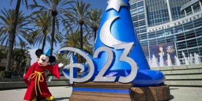 Mickey Mouse, dressed in his iconic red robe, greets fans beside a giant “D23” sign and the famous blue sorcerer hat outside the convention center, setting a magical tone for Disney’s unforgettable D23 Fan Event in California.