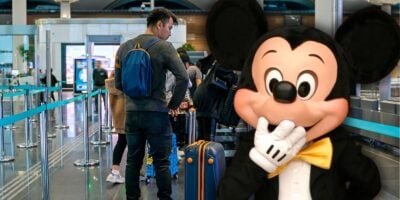 Mickey Mouse greets guests at Disney World, flashing his signature smile as visitors line up nearby in the airport-style queue.