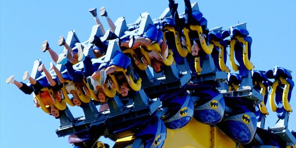 Thrill-seekers soar upside down on the twisted tracks of the Steel Vortex inverted coaster, legs flailing high against a backdrop of clear blue sky.