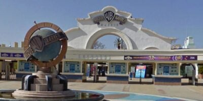 Parque Warner Madrid entrance featuring colorful ticket booths and the iconic WB logo statue welcoming guests.
