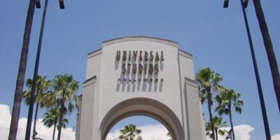 Universal Studios Hollywood’s famous entrance arch welcomes guests, surrounded by soaring palm trees and set against a bright blue California sky.