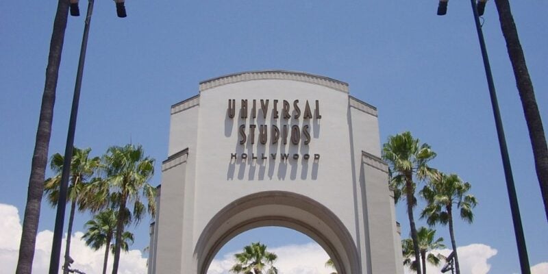 Universal Studios Hollywood’s famous entrance arch welcomes guests, surrounded by soaring palm trees and set against a bright blue California sky.