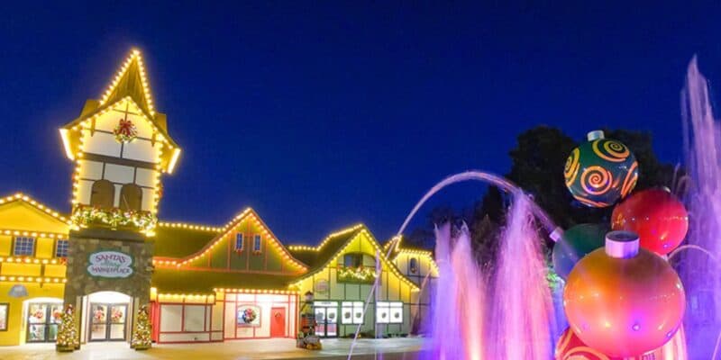 Holiday lights twinkle across iconic park buildings, while vibrant fountains dance and oversized ornaments sparkle throughout the grounds at night, creating a festive wonderland that brings the theme park’s magic and excitement to life during the holiday season.
