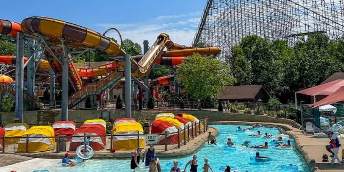 Guests float along the lazy river surrounded by vibrant water slides and a towering roller coaster at a bustling American theme park, all while experiencing smooth and uninterrupted park entertainment.