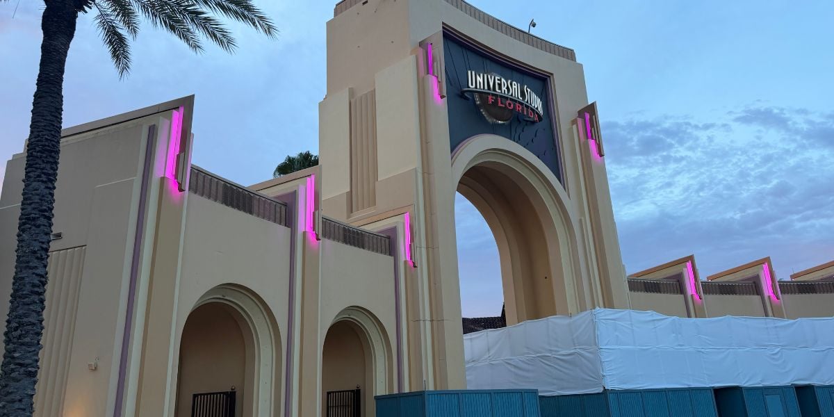 Universal Studios Florida entrance arch illuminated with pink lights at dusk, with construction barriers in front as guests arrive for an evening of thrills.