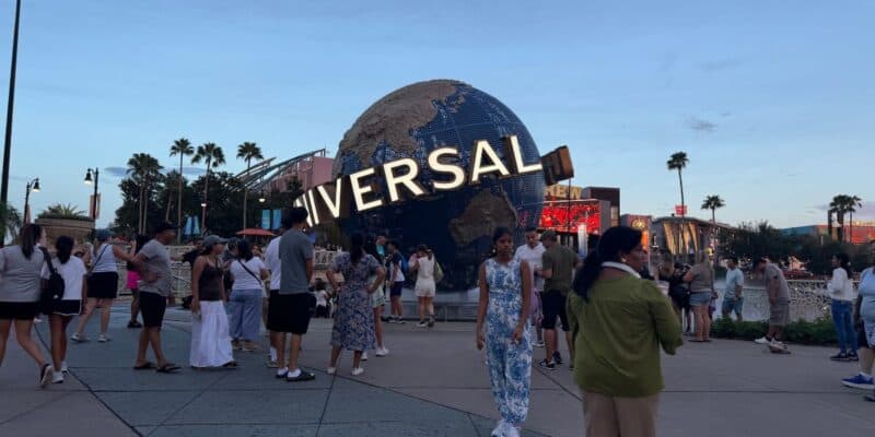 Excited guests surround the iconic Universal globe at the entrance to Universal Studios on a sunny day, ready for an action-packed adventure.