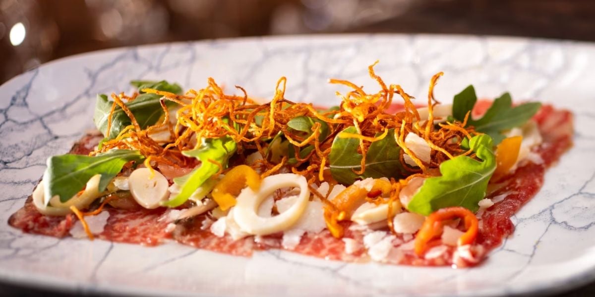 A vibrant entrée of thinly sliced beef loaded with colorful greens, crispy fried onions, cheese shavings, and fresh veggies, all artfully arranged on a whimsical plate—perfect fuel for an epic day of rides and shows at the park.
