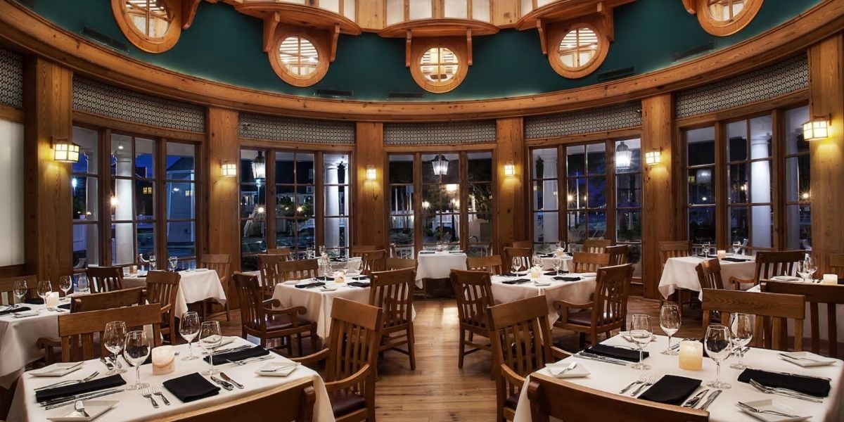 Whimsical round dining room inspired by theme park magic, featuring wooden chairs, crisp white tablecloths, and golden ambient lighting, perfectly set for an immersive dinner after a day of attractions.