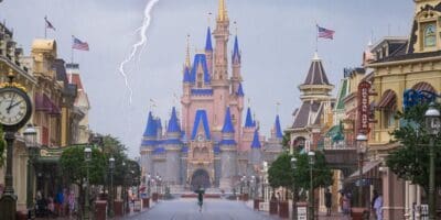 Guests walk through Walt Disney World in rain with a recognizable theme park landmark visible in the background.