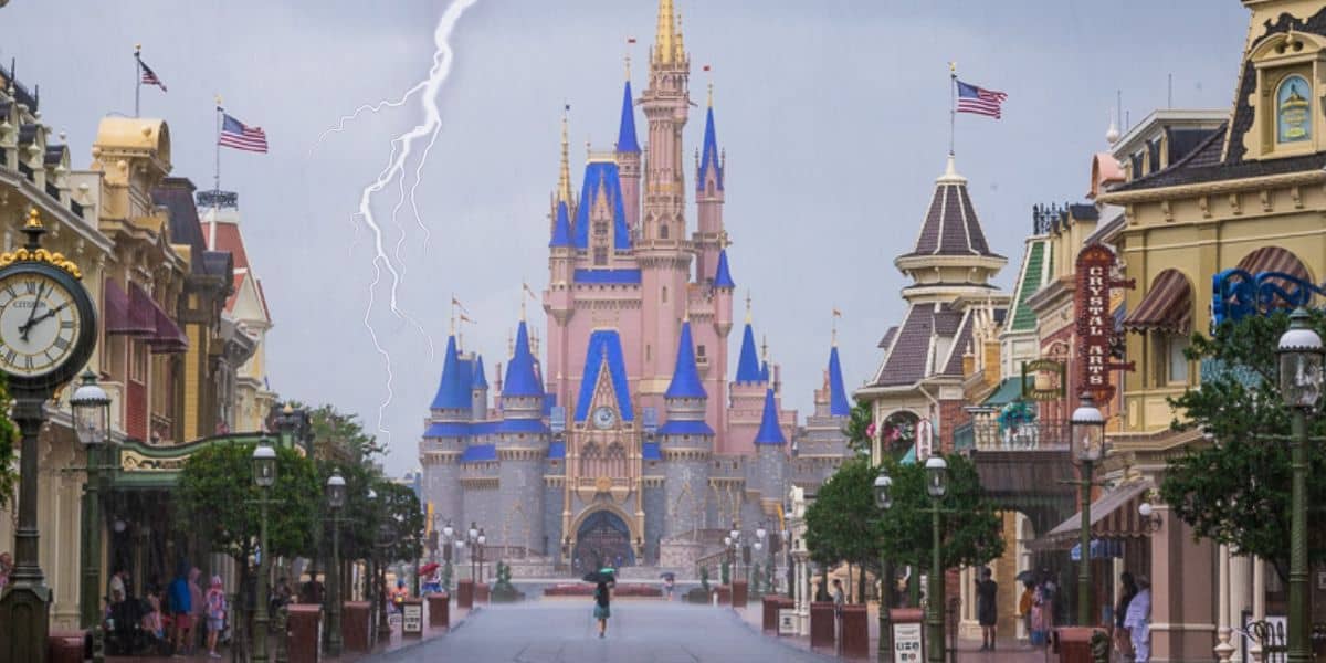 Guests walk through Walt Disney World in rain with a recognizable theme park landmark visible in the background.