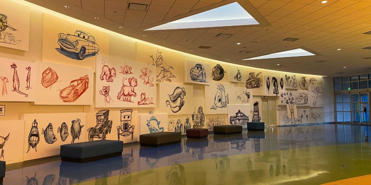 A colorful corridor adorned with playful cartoon sketches along the walls and benches lining the gleaming floor, capturing the lively atmosphere and creative flair of Disney World’s Art of Animation Resort.