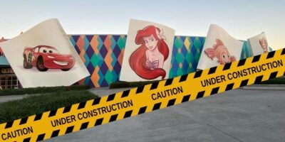 Caution tape cordons off a vibrant mural of animated favorites on the exterior wall of a theme park attraction, signaling ongoing enhancements.
