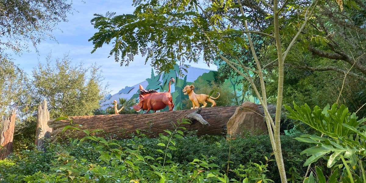 Simba, Timon, and Pumbaa strike a classic pose atop their log in the lush outdoor setting of Disney World’s Art of Animation Resort, surrounded by vibrant greenery and playful landscaping.
