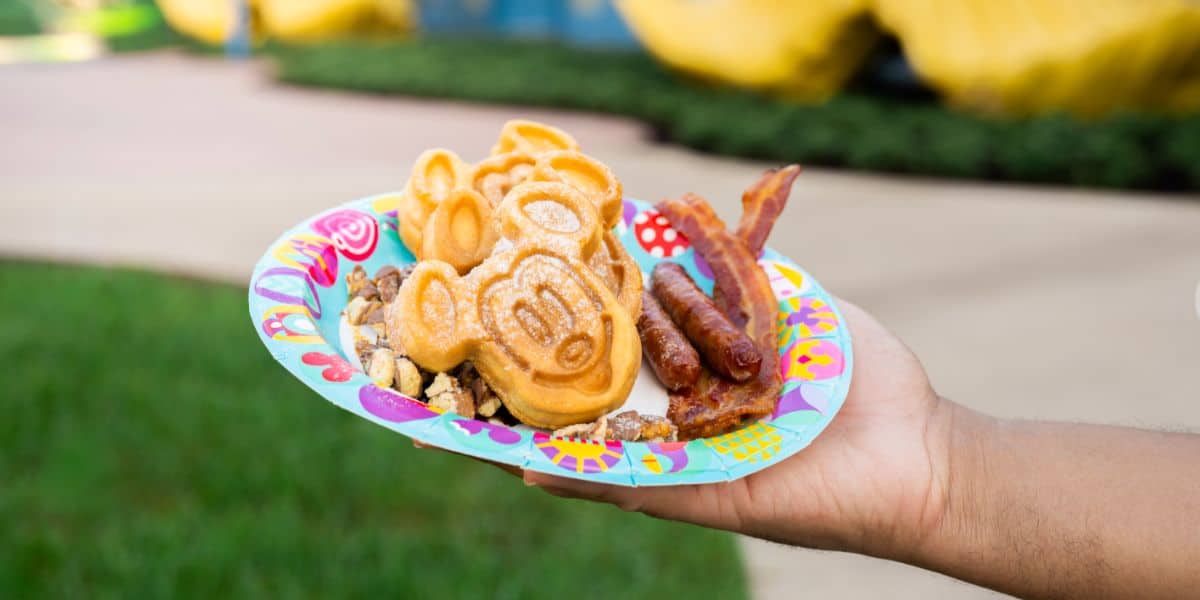 Mickey-shaped waffles served with bacon and sausage on a plate, ready to enjoy outdoors at Disney World.