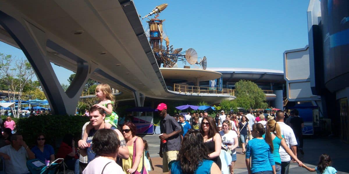 Excited guests stroll through EPCOT beneath a vibrant blue sky, surrounded by the park’s iconic futuristic pavilions.