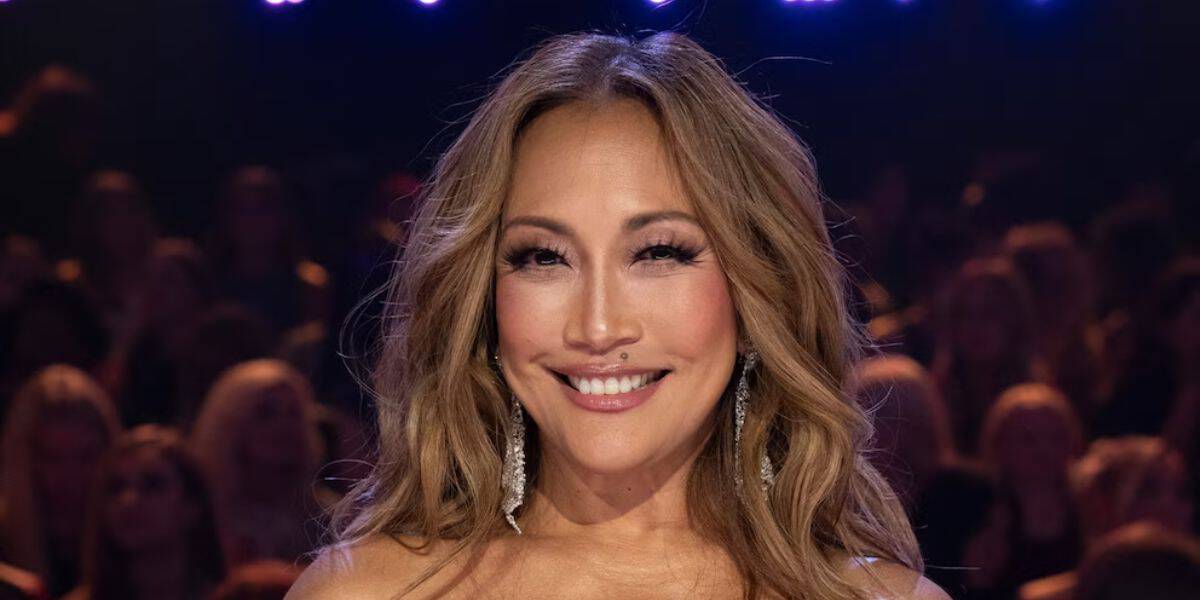 Carrie Ann Inaba beams with a warm smile, her signature long wavy hair and sparkling earrings catching the stage lights, as she stands before a blurred audience on Dancing With The Stars, ready to share her expert critique with fans eagerly watching.