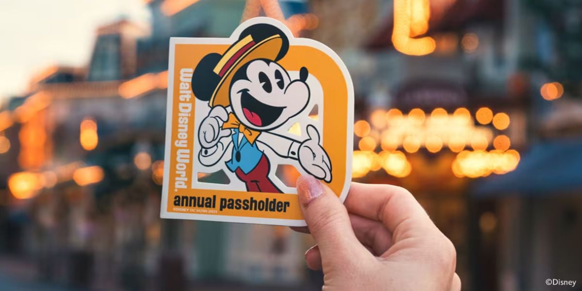 A Walt Disney World annual passholder sticker with Mickey Mouse is showcased, with the park’s magical lights softly glowing in the background.