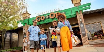 A joyful family exits a Disney store, their hands full of iconic character plushies and themed shopping bags, savoring the magic of the Disney Parks experience.