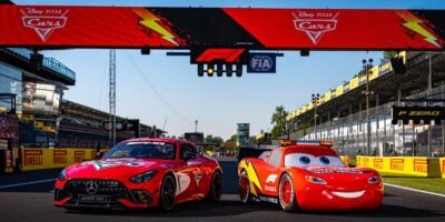 Lightning McQueen from Disney-Pixar’s Cars and a red Mercedes-AMG safety car are on display together on a Formula 1 racetrack, creating an exciting photo opportunity for fans at a motorsports-themed park experience.