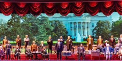 The Hall of Presidents stage features lifelike wax figures of U.S. presidents set against a grand White House backdrop, framed by dramatic red curtains.