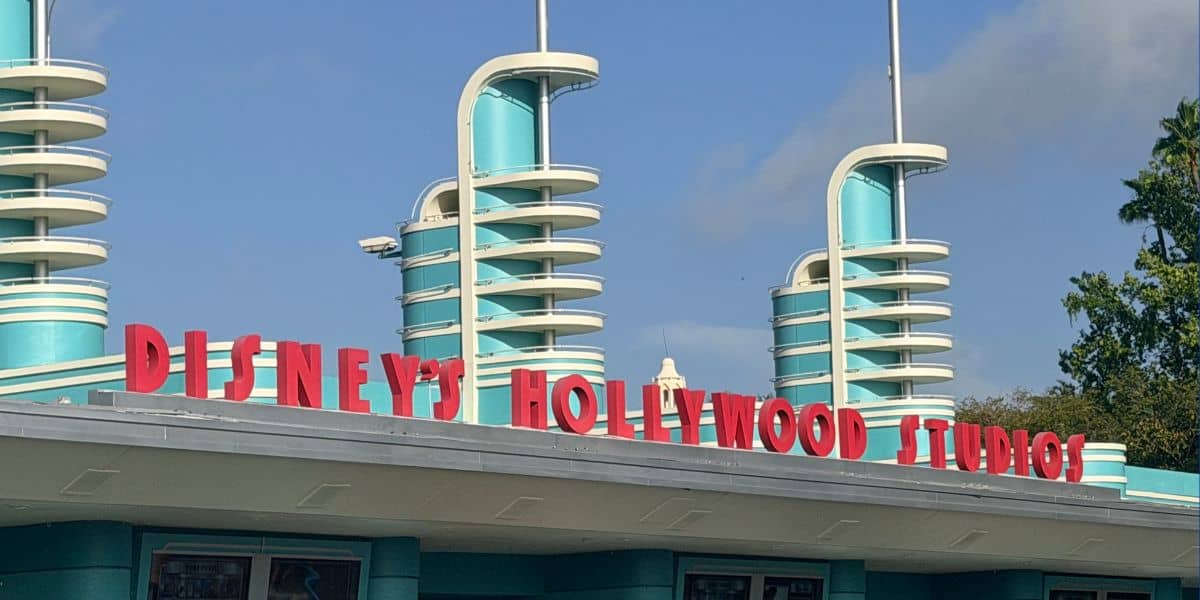 The iconic entrance to Disney’s Hollywood Studios, featuring classic teal art deco towers and bold red lettering, welcomes guests under a vibrant blue sky.