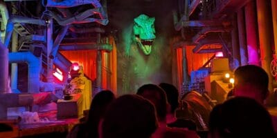 Guests on a Jurassic Park River Adventure raft approach the massive green-lit animatronic T. rex head inside the ride