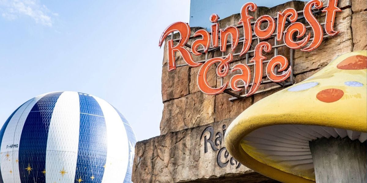 Rainforest Cafe sign set against a rugged rock wall, with colorful themed decor including a striped hot air balloon and an oversized yellow mushroom creating an immersive, adventure-filled atmosphere.