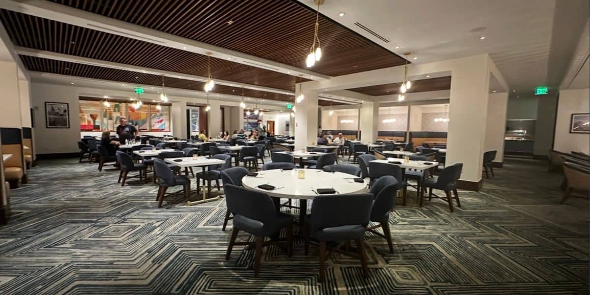 Vibrant theme park restaurant featuring round tables, bright blue chairs, and guests enjoying their meals amid energetic park atmosphere.