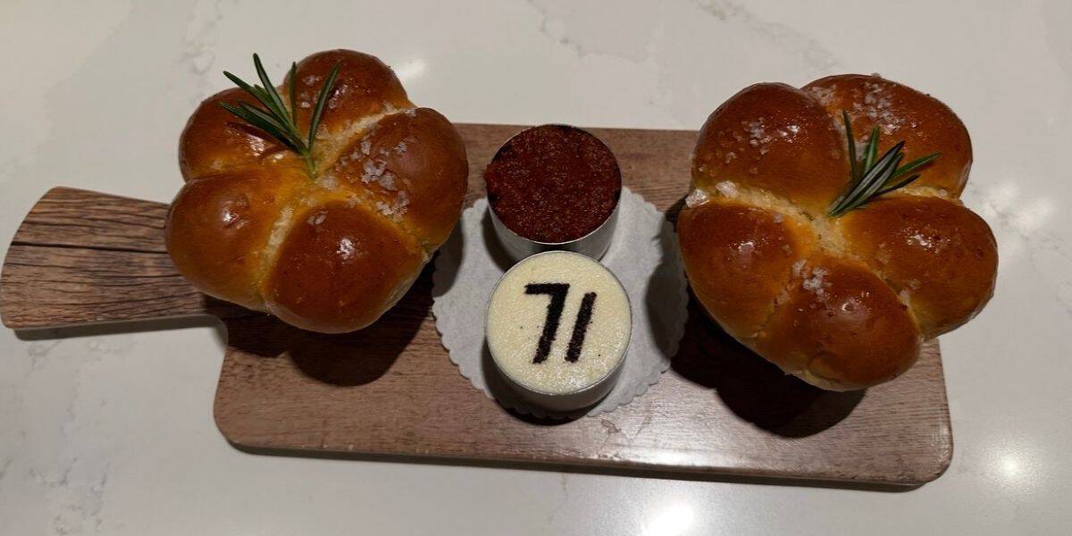 Fresh rosemary-topped bread rolls and two celebratory mini cakes—one decorated with a bold “71”—served on a rustic wooden board, as featured at Walt Disney World’s 71st anniversary event.