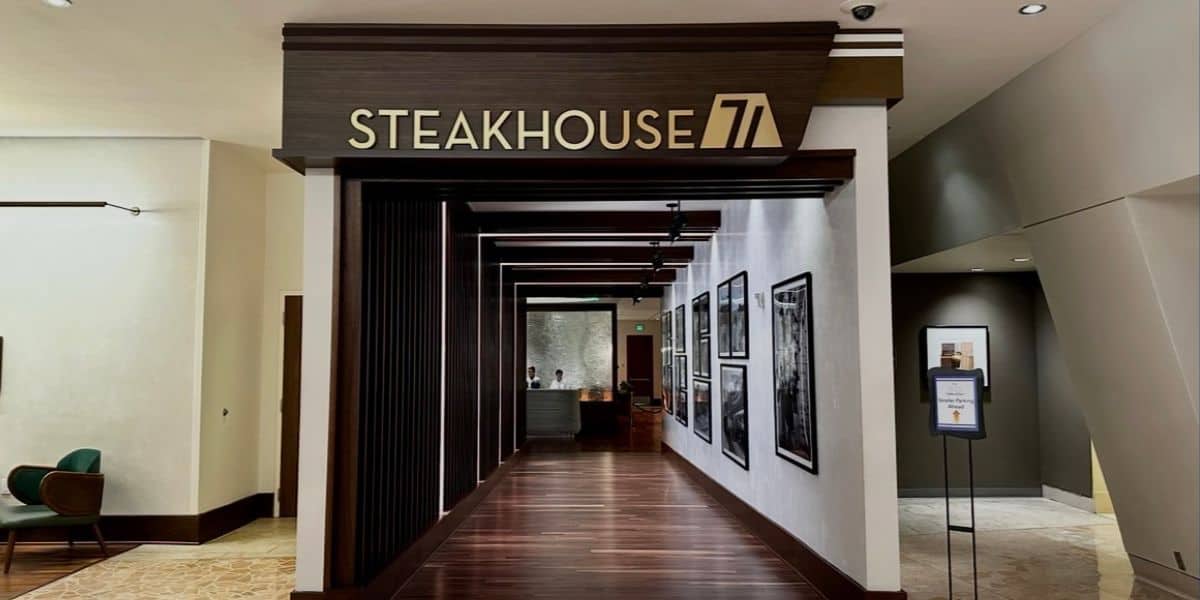 Entry hallway leading to Steakhouse 71 at Disney’s Contemporary Resort, lined with framed photos celebrating Disney history, and a hostess stand welcoming guests at the end.