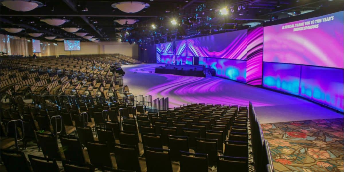Spacious event venue with theater-style seating, illuminated stage with vibrant purple lights, and a dynamic digital display—ready for an exciting live entertainment show or theme park presentation.