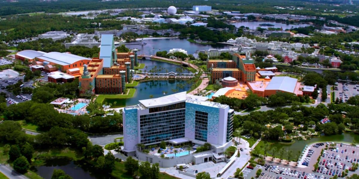 Aerial view of a sprawling entertainment resort featuring themed hotel buildings, sparkling pools, and expansive parking lots nestled amid lush landscaping.
