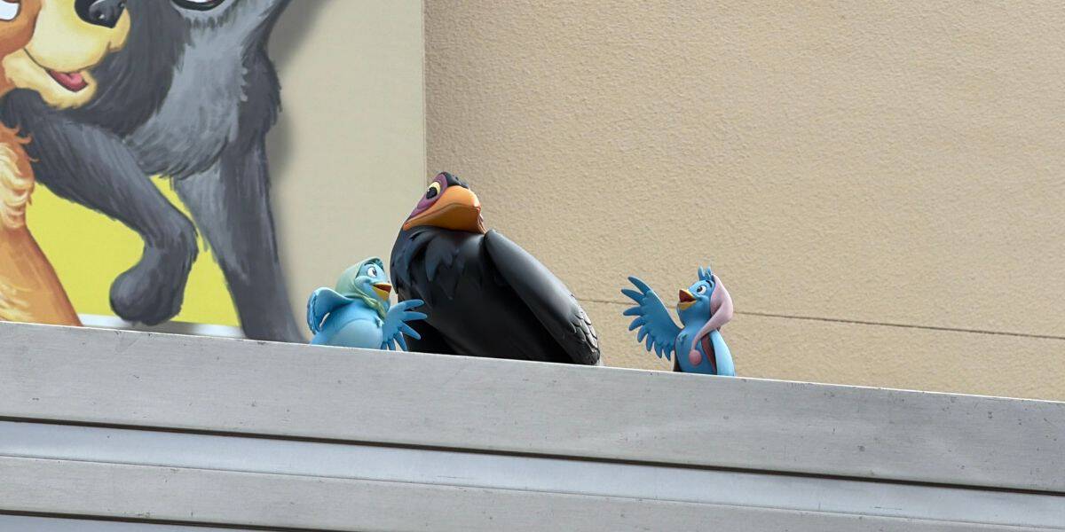 Three whimsical bird statues from Disney’s Hollywood Studios perch on a ledge, backed by a vibrant, partially visible animal mural that adds extra magic to the park atmosphere.