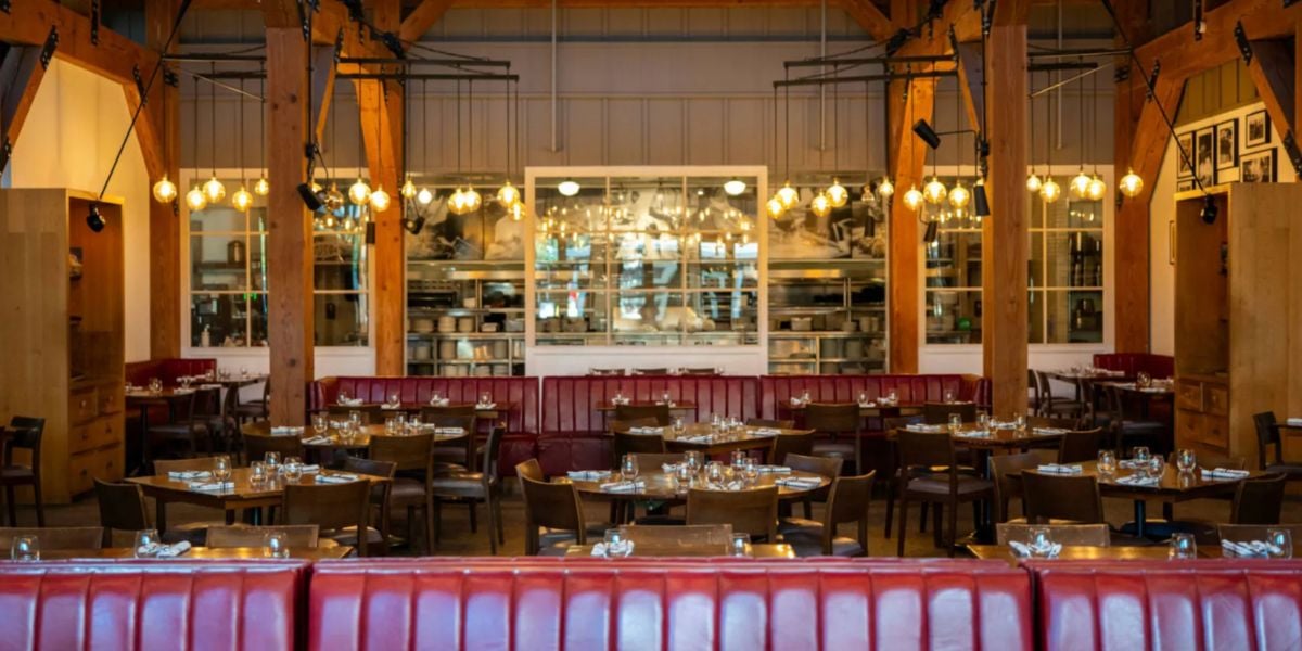 A vibrant, welcoming restaurant with classic red booths, polished wooden tables, and glowing overhead lights, styled for guests ready to enjoy a meal in an atmosphere that echoes the lively dining experiences once found at Wolfgang Puck in Disney Springs before it closed.