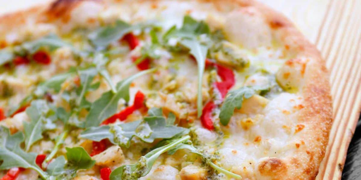 Artisan pizza topped with arugula, red peppers, and pesto served at the park.