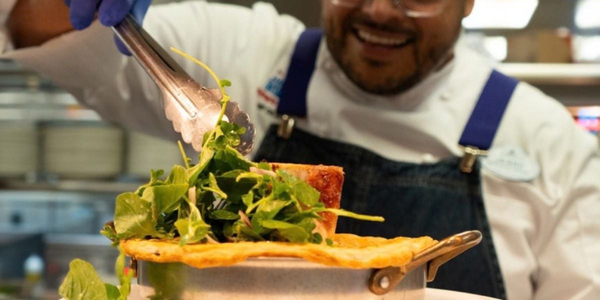 A Chef de Cuisine garnishing a dish with greens in a Magic Kingdom kitchen.