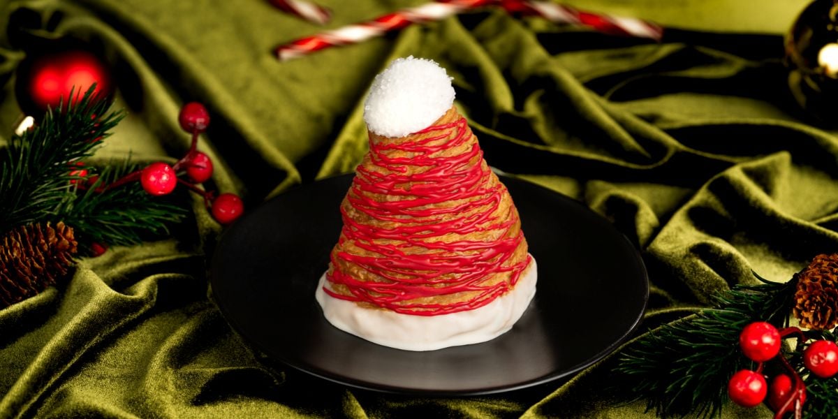 A Santa hat-shaped pastry drizzled with red icing, served on a black plate.