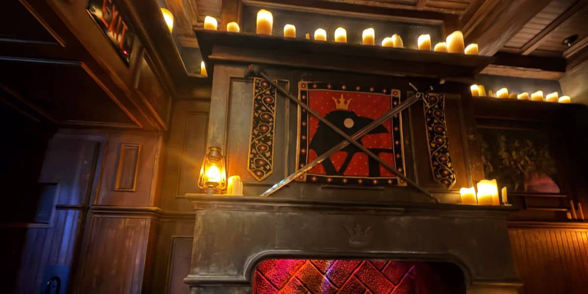 Fireplace with a raven crest and crossed swords at Gaston’s Tavern in Magic Kingdom, reminiscent of the Six Ravens decor.